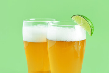 Glasses of cold beer with lime on green background