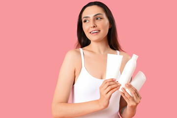 Young woman with bottles of sunscreen cream on pink background