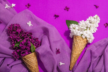 White and violet lilac flowers in waffle ice cream cones on purple background. Flat lay