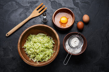 Bowls with ingredients for preparing zucchini fritters on black background