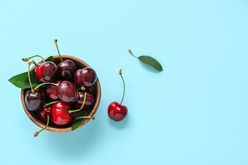 Bowl with sweet cherries on blue background