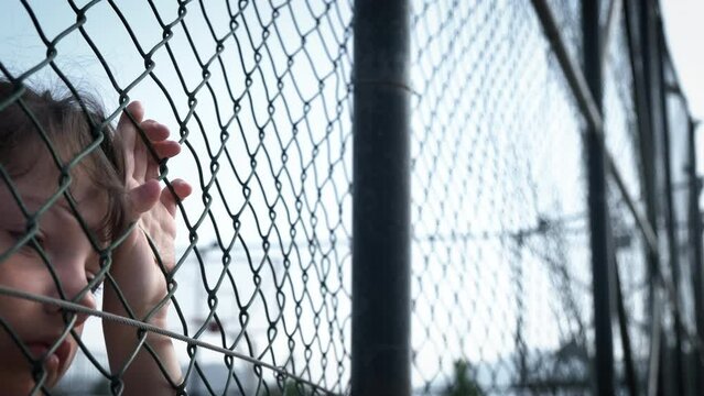 Children behind the fence. Little girls look fearfully through the wire fence.