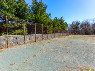 Old abandoned green clay tennis court with galvanized chain link fence.
