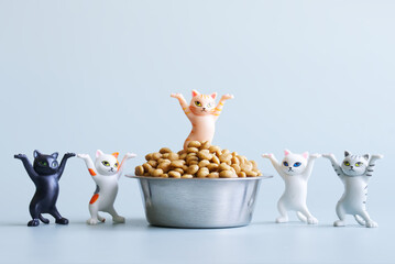 Five funny toy dancing kittens with raised paws next to a bowl filled with dry cat food. The...