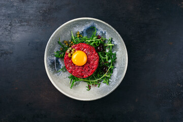 Modern style gourmet tartar raw from beef filet with egg, rucola and capers served as top view on a...