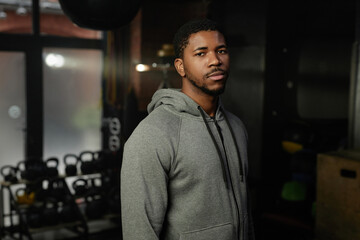 Young serious African American man in grey activewear standing in front of camera in spacious gym or modern leisure center and looking at you