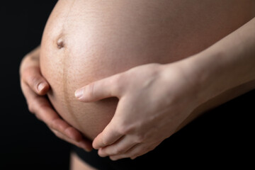 Closeup of naked round belly held by hands of pregnant woman in underwear. Last month of pregnancy...