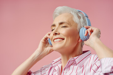 Happy senior woman with eyes closed listening music in wireless headphones