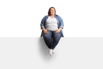 Young overweight woman sitting on a blank panel - obrazy, fototapety, plakaty