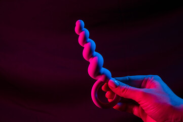 Woman holding anal beads in neon pink blue light. Copy space. 