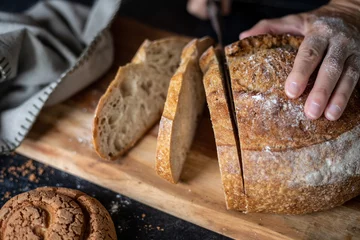 Schilderijen op glas person slicing a loaf of bread on a board, close up, focus on the slice of bread © PetraJPhoto