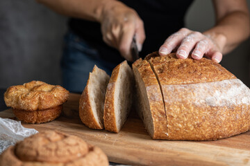 person cutting a loaf of bread on the table, space for text, focus on the bread - obrazy, fototapety, plakaty