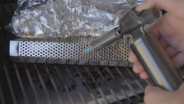 This video shows a flaming torch being used to ignite a bbq pellet basket in a smoker grill.