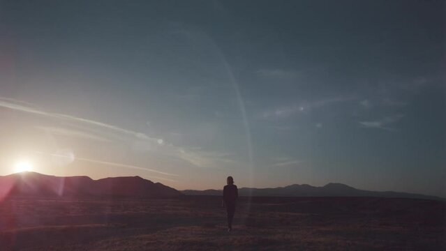 Man with long hair walking accross the desert with purple lens flare. Alien planet
