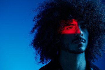 Fashion portrait of a man with curly hair on a blue background, multinational, colored light, trendy, modern concept.