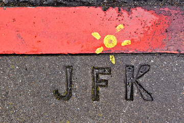 Painted Sun honors JFK.  JFK initials on sidewalk next to red curb with painted sun, John F. Kennedy Drive, San Francisco, California 