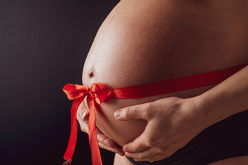 Side angle closeup of naked round belly with a tied red bow. Last month of pregnancy - week 36....