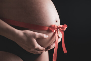 Side angle closeup of naked round belly with a tied red bow. Last month of pregnancy - week 36....
