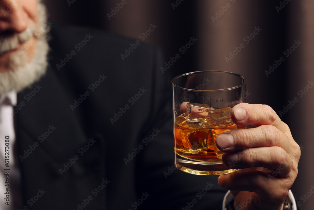 Wall mural Man holding glass of whiskey with ice cubes on dark background, closeup