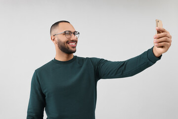 Fototapeta premium Smiling young man taking selfie with smartphone on grey background