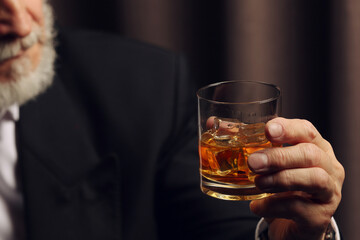Man holding glass of whiskey with ice cubes on dark background, closeup