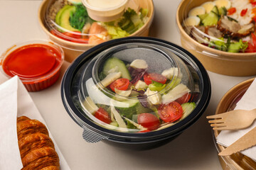 Tasty food in containers with wooden knife and fork on light grey table
