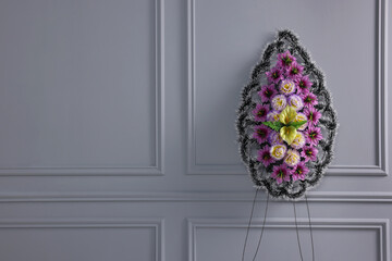 Funeral wreath of plastic flowers near light grey wall, space for text