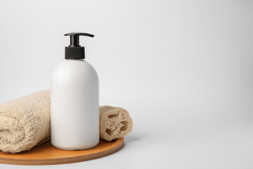 Fototapeta na wymiar Bottle with cosmetic product, rolled towel and loofah sponge on white background. Space for text