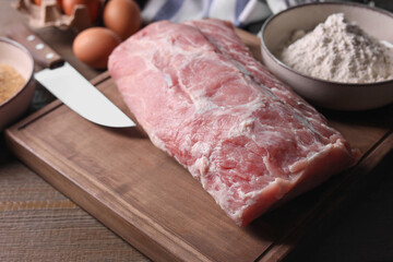 Fresh pork meat and other ingredients for cooking schnitzel on wooden table, closeup
