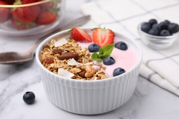 Tasty granola, yogurt and fresh berries in bowl on white marble table, closeup. Healthy breakfast