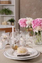 Stylish table setting with beautiful peonies and burning candles indoors