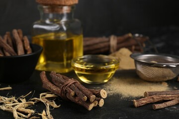 Dried sticks of licorice roots, powder and essential oil on black table. Space for text