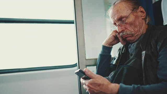 Senior with glasses uses mobile phone while traveling in train coupe