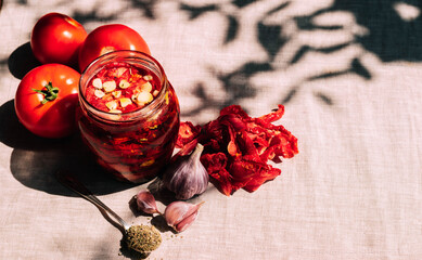 Dried tomatoes with spices in a jar, various spices and herbs lie on the kitchen table, bright...