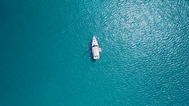 A sailboat floating stil in some clear blue water, aerial view with long distance, yacht at mediterranean sea, island of mallorca, playa de es tranc, caribbean beach, tropical summer vibes, travel