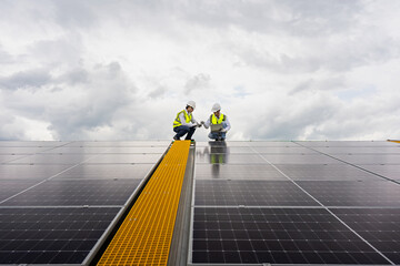 Two young Asian engineers checking the installation of solar panels on the factory roof, checking...