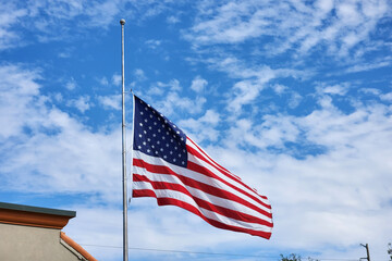 USA national flag waving lowered to half mast on wind against blue sky. American stars and stripes...