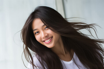 Charming Asian teenager with long hair blowing in the breeze exudes positivity with a bright smile on a white background.