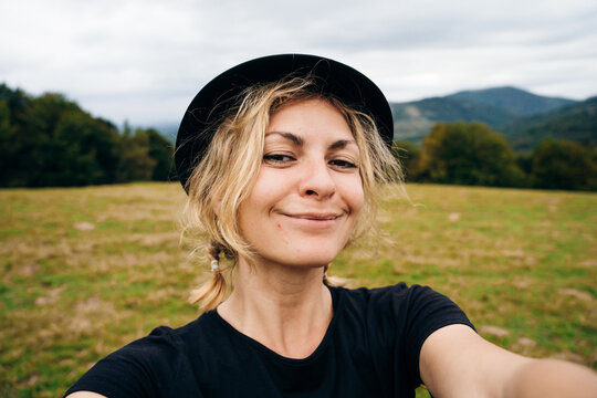young blonde girl takes a selfie in a black hat and t-shirt