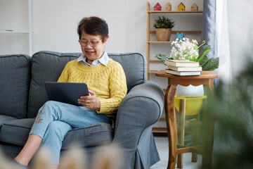 Mature Asian Woman Using Digital Tablet Sitting At Home