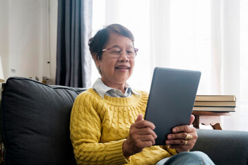 Mature Asian Woman Using Digital Tablet Sitting At Home