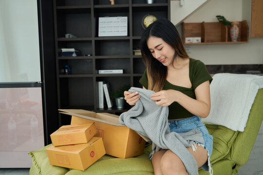 Young asian women unpacking awaited parce looking inside, sitting at sofa, unhappy customer opening cardboard box with online store order,Delivery service concept.