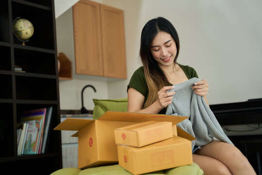 Young asian women unpacking awaited parce looking inside, sitting at sofa, unhappy customer opening cardboard box with online store order,Delivery service concept.