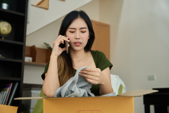 Young asian women unpacking awaited parce looking inside, sitting at sofa, unhappy customer opening cardboard box with online store order,Delivery service concept.