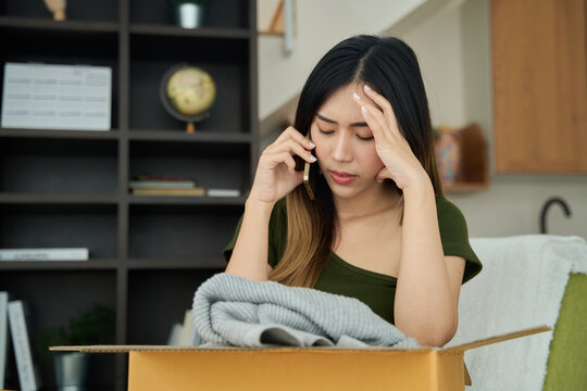Young asian women unpacking awaited parce looking inside, sitting at sofa, unhappy customer opening cardboard box with online store order,Delivery service concept.