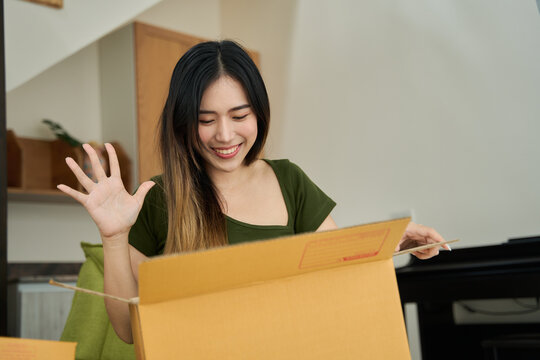 Young asian women unpacking awaited parce looking inside, sitting at sofa, satisfied happy customer opening cardboard box with online store order, smiling laughing celebrating success.