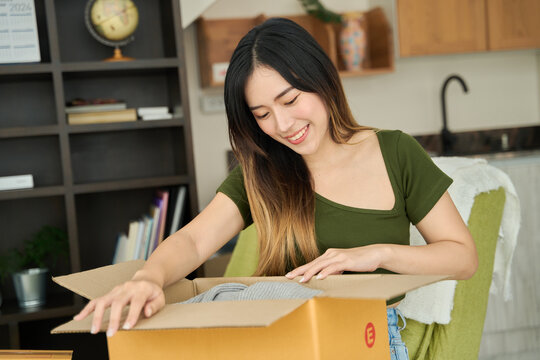 Young asian women unpacking awaited parce looking inside, sitting at sofa, unhappy customer opening cardboard box with online store order,Delivery service concept.