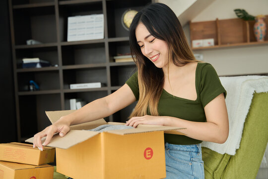 Young asian women unpacking awaited parce looking inside, sitting at sofa, unhappy customer opening cardboard box with online store order,Delivery service concept.