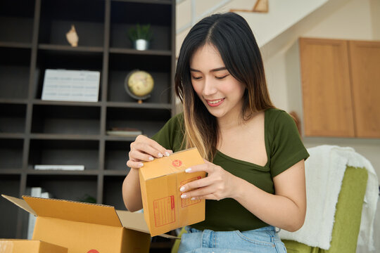 Young asian women unpacking awaited parce looking inside, sitting at sofa, unhappy customer opening cardboard box with online store order,Delivery service concept.