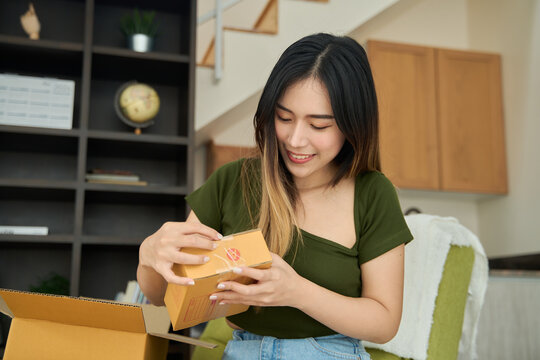 Young asian women unpacking awaited parce looking inside, sitting at sofa, unhappy customer opening cardboard box with online store order,Delivery service concept.